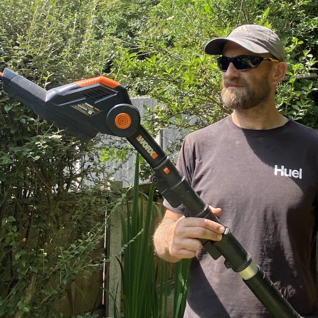 Man using Worx cordless hedge trimmer next to PowerShare compatible tool types list